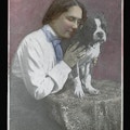 Helen Keller, seated to left of table facing right, with hand and face on Boston terrier Phiz, which is sitting on table.