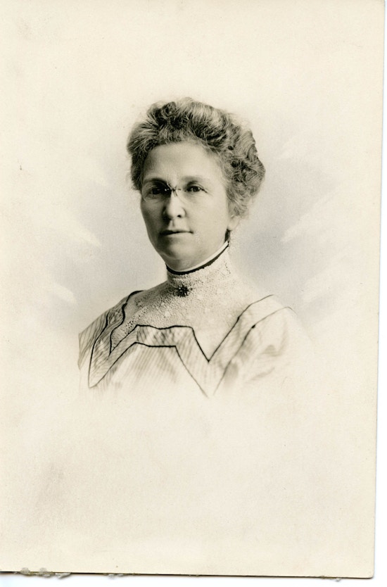 A head and shoulders portrait of a Horace Mann School female oral educator with glasses and a curled up-do hair style.