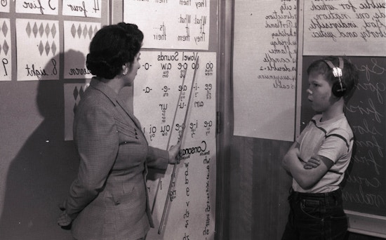 Teacher pointing to symbols printed on a large sheet of paper, facing side right.