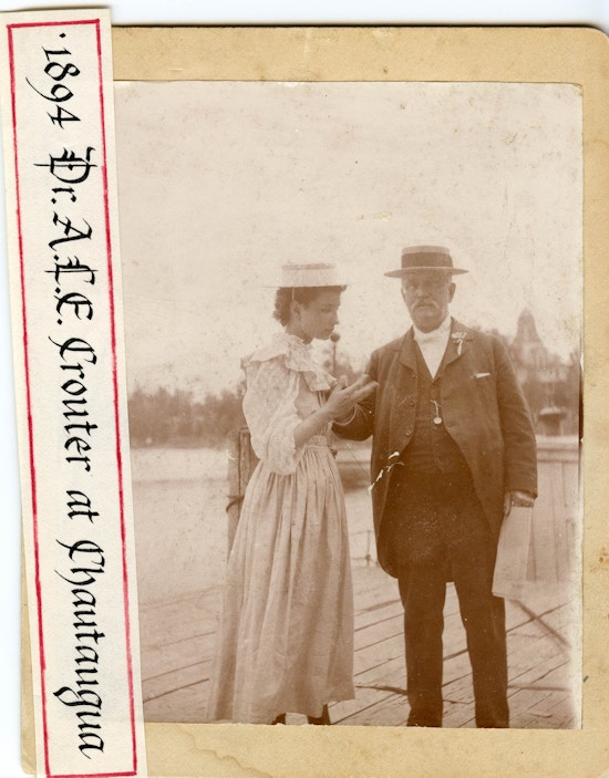 Helen Keller in lightly colored dress wearing a hat and to the left of Dr. A.L.E. Crouter, wearing a suit and hat, at Chautauqua.