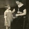 Helen Keller (right), seated, holding a bouquet of flowers, with child, standing.