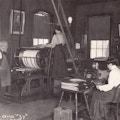 One man with apron, two women in light blouses and dark skirts, printing equipment.