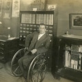 Man using wheelchair in an office, another man at a desk.