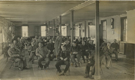 About forty men sitting in a hall.