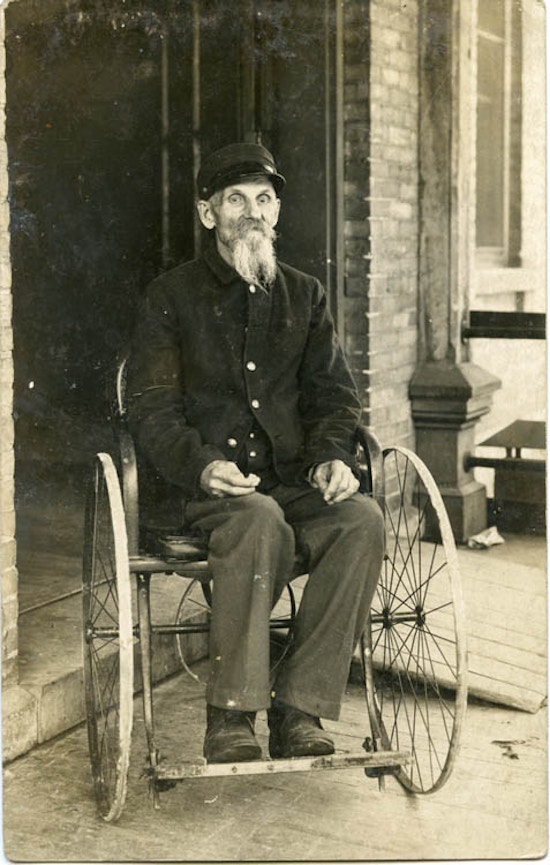Bearded man sitting in wheelchair, ramp in background.