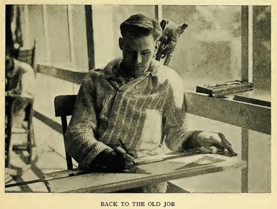 Young man sits working at drafting board,