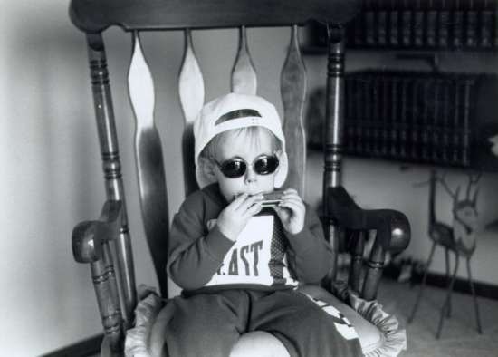 A young boy wearing sunglasses plays a harmonica.