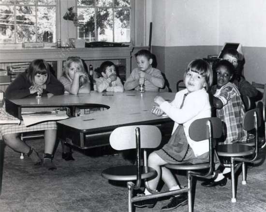 Seven children sit at a table.  Three of the children have Down Syndrome.