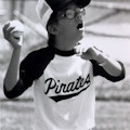 A with glasses wearing a baseball uniform prepares to throw a baseball.