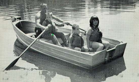 Photograph of young man helping a boy row a rowboat.  Two girls are also in the boat.