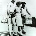 Two veterans with prosthetic legs use a nurse for support as the three rollerskate.