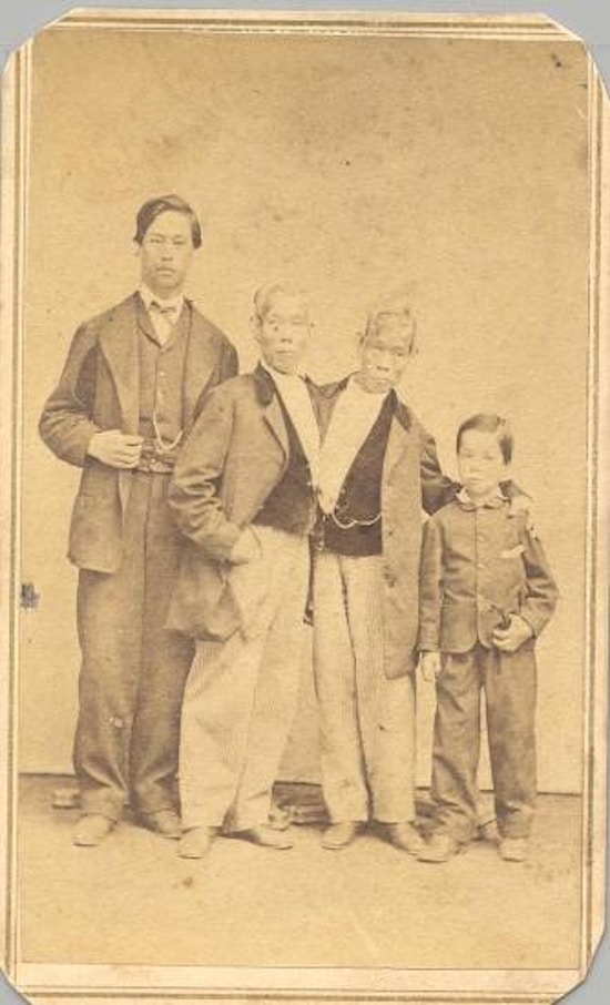 Chang and Eng stand between a young man and a boy.