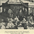 A group of children with presents, surrounded by adults, one dressed as Santa Claus.