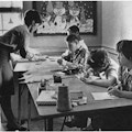 A woman helping four children working on art.