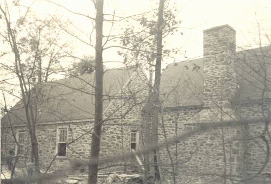 A stone house during construction, seen through trees.