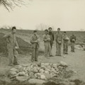 Seven young men and boys stand by a pile of rocks.