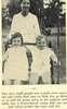 Two children sit in a swing with a nurse standing behind them.
