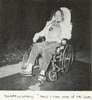 A woman in wheelchair and wearing a chestliece plays shuffleboard.