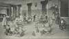 Childern in a large room, some sitting and others standing.