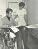 A man in a wheelchair and a nurse look at papers.