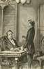 A man speaks with another sitting at a desk.