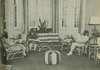 Three women sits in a couch and chairs.  The rooms has a lamp, curtains, and plants.
