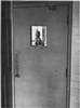A man seen through the barred window of a door.