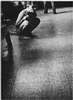 A naked young man crouching on a stone floor.