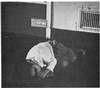 An African-American boy lying on the floor next a metal door.