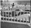 A child lying in bed with side rails in a room filled with identical beds.