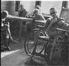 Men in a ward, some around a table, one in a wheelchair.