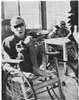 Men on a ward, one in a wheelchair, others on a wooden bench.