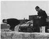 Two young men with rocks gathered in a cart next to a stone wall.