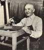 An elderly man varnishing a chair.