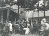 Group sitting on chairs next to Top Cottage porch.  A line of people leads to porch entrance.