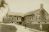 Two boys stand before a shingled building.