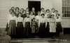 Photograph of girls and male teacher on front steps of school building.  One of the girls is short-statured.