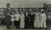 Photograph of eight short-statured people standing in line, arms interlocked, dressed in formal wear.