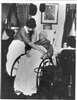 Elderly woman in wheelchair, with blanket over her legs, is tended by nurse.