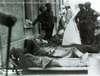 Soldiers lying on stretchers; nurse and officers in background