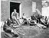 Soldiers sit or lie on the ground in an outdoor courtyard. A nurse helps a soldier on crutches out the door.