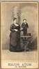 Major Atom, holding a top hat, stands on a table next to an average sized woman.