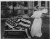 A woman signs next a flag draped over a bench.