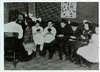 A group of seven children and their teacher speak while looking into mirrors.