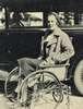 A woman sits in a wheelchair next to a car.