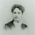 Young Sullivan facing camera, curly hair, dark dress, white lace collar with dark broach at throat.