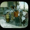 Lantern slide showing women and children with empty large pans. One woman is receiving a full pail of coal. Probably in NY