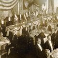 Group of formally dressed men at banquet.