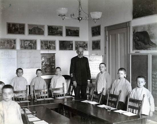 Horace Mann students and teacher stand behind desks and chairs, facing the camera in a classroom.