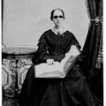 Bridgman, seated facing camera, holding book, dark dress with lace collar, dark glasses.